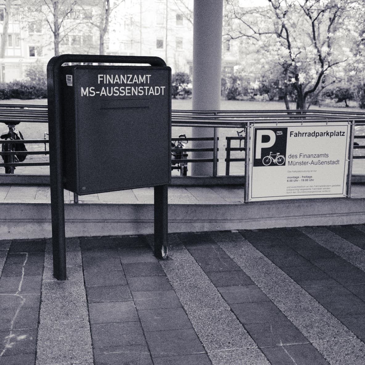 Official letterbox reading “Finanzamt MS-Außenstadt” beside a bicycle-parking sign.