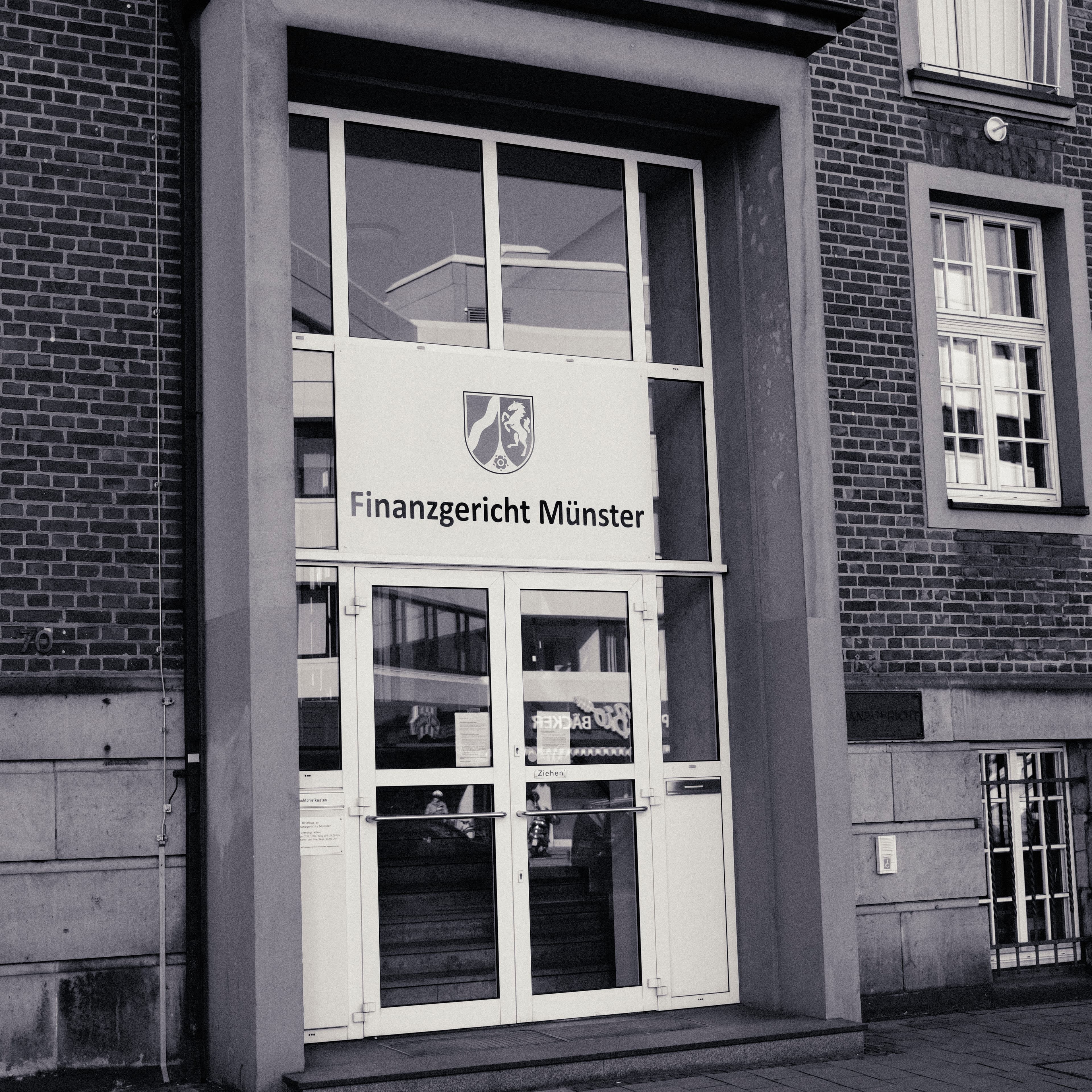 Entrance portal of the Münster Tax Court with the coat of arms of North Rhine-Westphalia and lettering above the glass door.