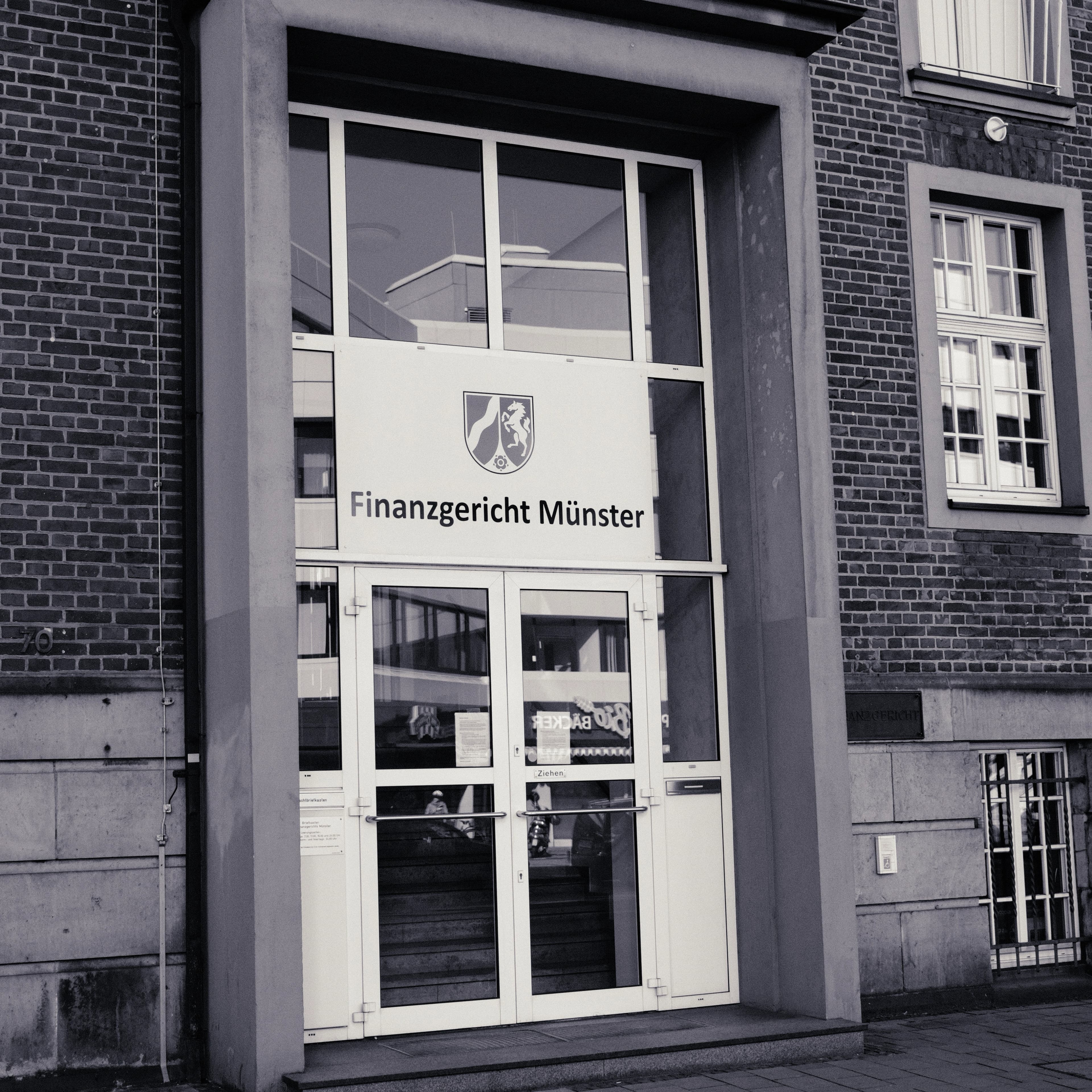 Eingangsportal des Finanzgerichts Münster mit Landeswappen Nordrhein-Westfalen und Beschriftung über der Glastür.