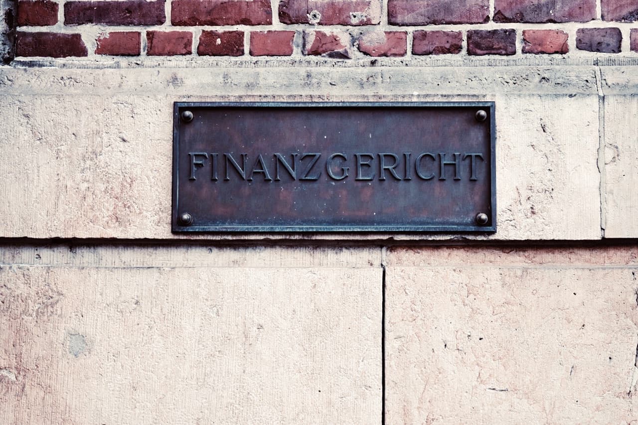 Weathered bronze plaque reading “Finanzgericht” on a sandstone and brick façade.