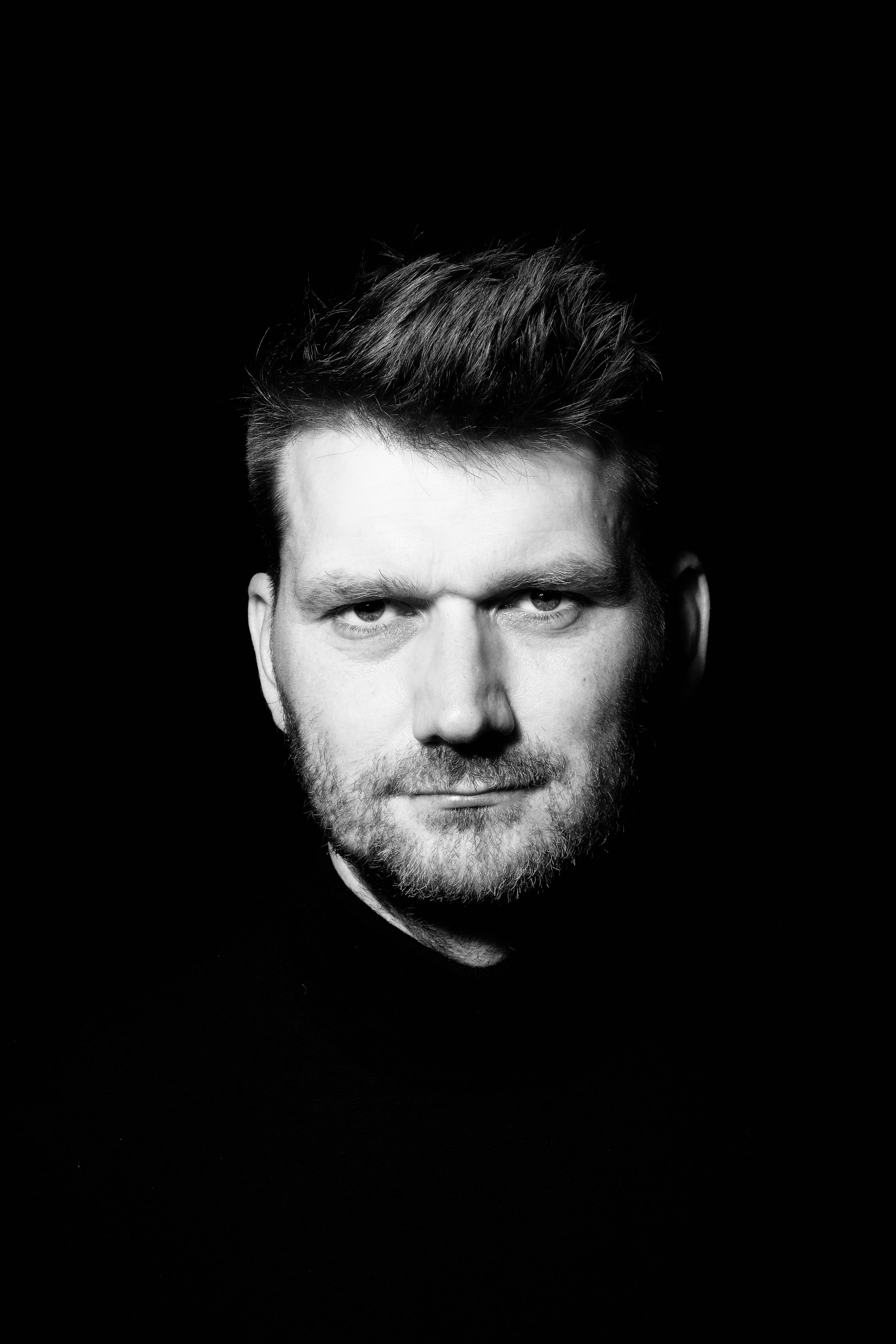 Hendrik Bruns, black-and-white portrait against a black background, looking into the camera.